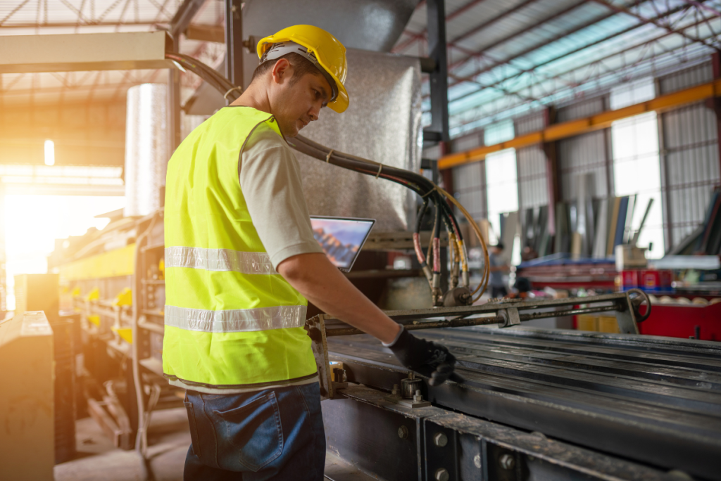 Factory worker in a safety vest and hard hat adjusts a metal conveyor on an assembly line in a factory.